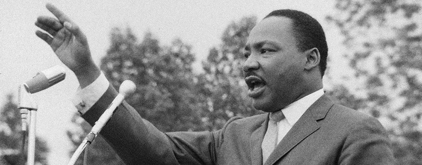 MLK standing with armed raised with two microphones in front of him