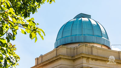 Melton Observatory on a sunny day with tree and gates mark.