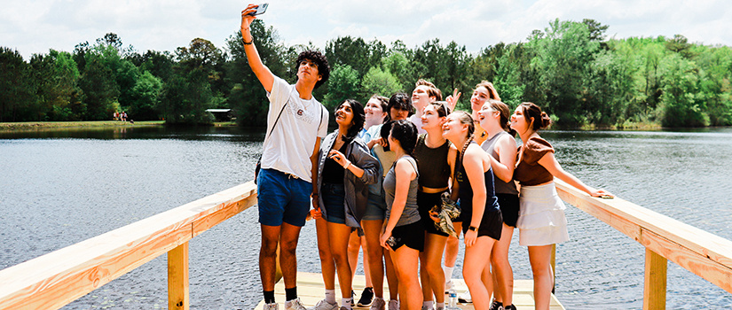 A group photo of students hold UofSC Top Scholar signs on the edge of Mission Lake