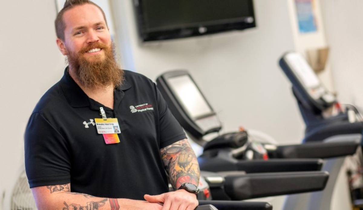 Male employee standing in front of exercise machines smiling. 