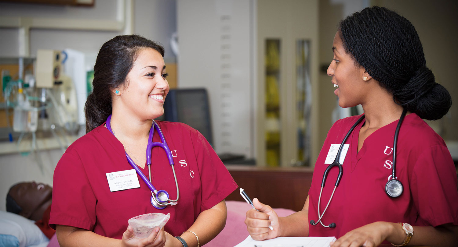 Two nurses talking together while writing in charts.