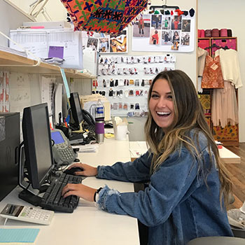 Student sitting at a desk at Free People with fabri samples and sketches around her. 