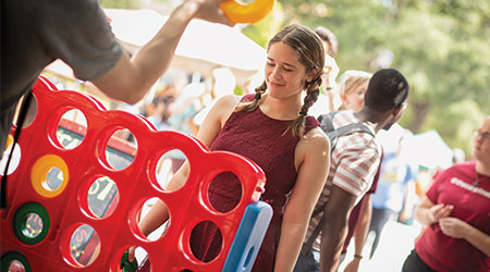 Student playing a large game of connect four on green street with other games going on around them. 