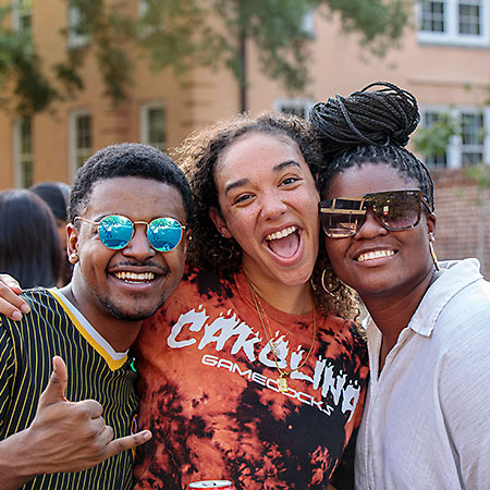 Three students posed together smiling holding a spurs up sign.