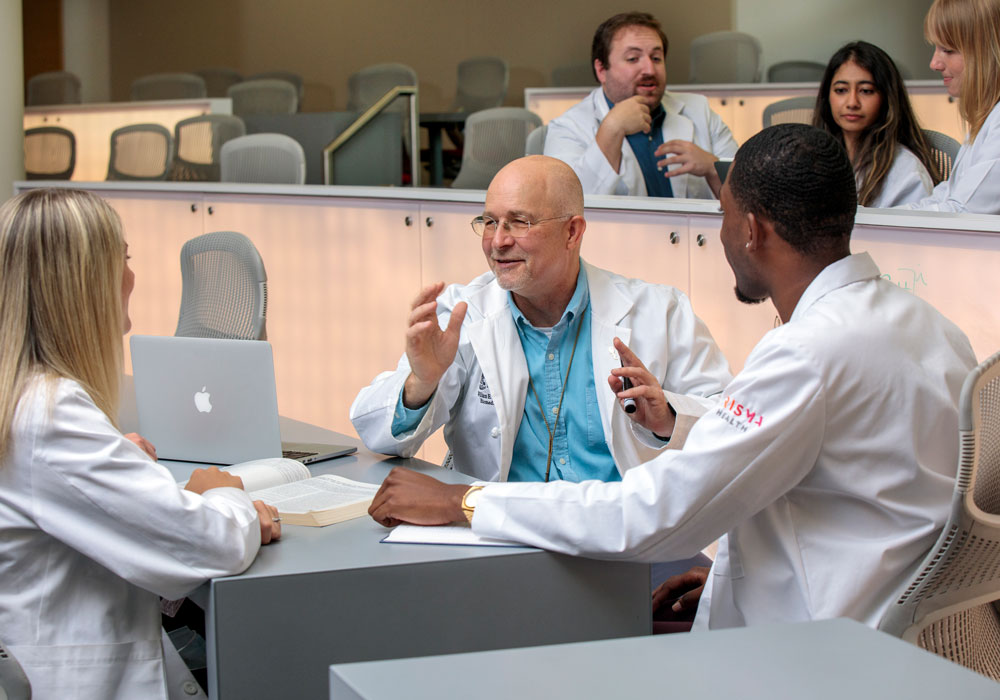 A professor  speaks to a group of students seated a table in a large classroom.