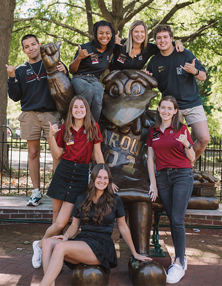 Group of ambassadors gathered around the Cocky Statue smiling at the camera.