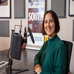 A photograph of Emily Allen, wearing a green top, while sitting in the Take on the South Podcast studio