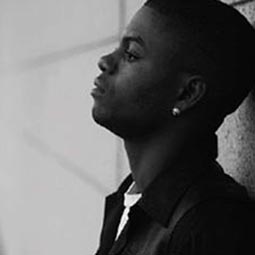 a black and white picture of a black man leaning against a cinderblock wall