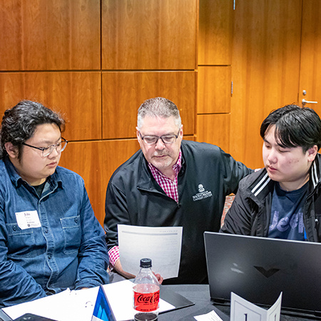 An instructor looks over a resume while two students look on.