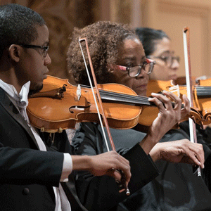 three musicians play violins on stage