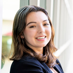 A headshot of Sarah Anne outside leaning against a wall and wearing a blazer