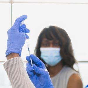 Doctor preparing a syringe and a woman with a face mask on is watching