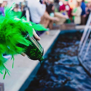 a hand pouring a bottle of green dye in a fountain