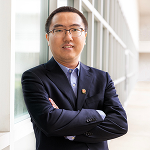 Chang Liu stands along a wall of windows