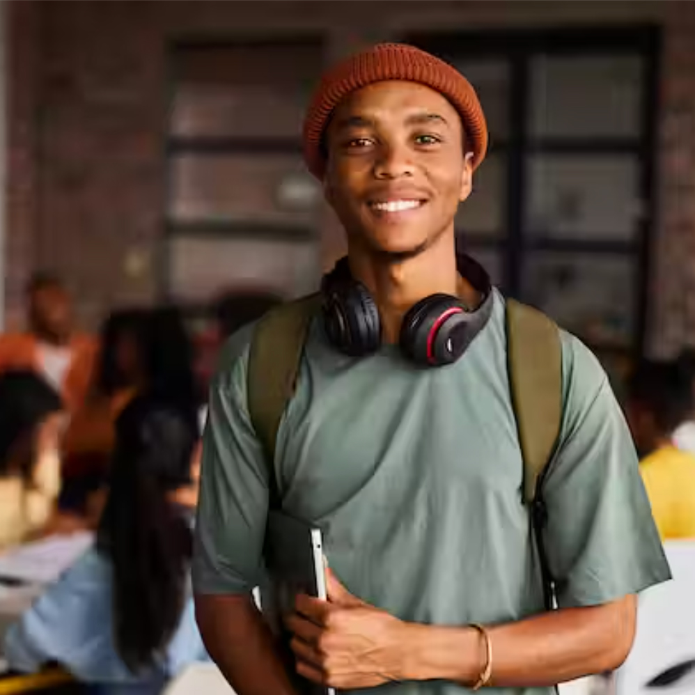 A man wearing a green shirt and orange hat with headphones around his neck smiles for the camera. 