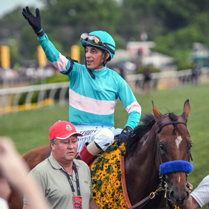 a jockey on horseback waves as two men walk beside the horse