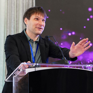 man speaks at a podium with a curtain in the background