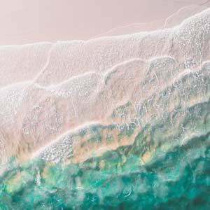 A drone image of a beach with teal blue water.