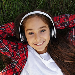 Adolescent girl wearing headphones, smiling and relaxing on grass field.