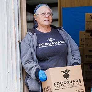 FoodShareSC volunteer carries a box of fresh produce.