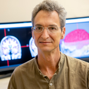 man sits in front of computer screens with brain images on display