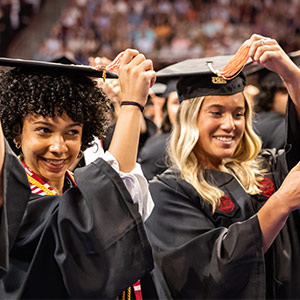 Two women in caps and gowns turning tassles on graduation caps