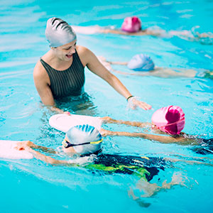 Children accompanied by an instructor swimming in a pool with kickboards 