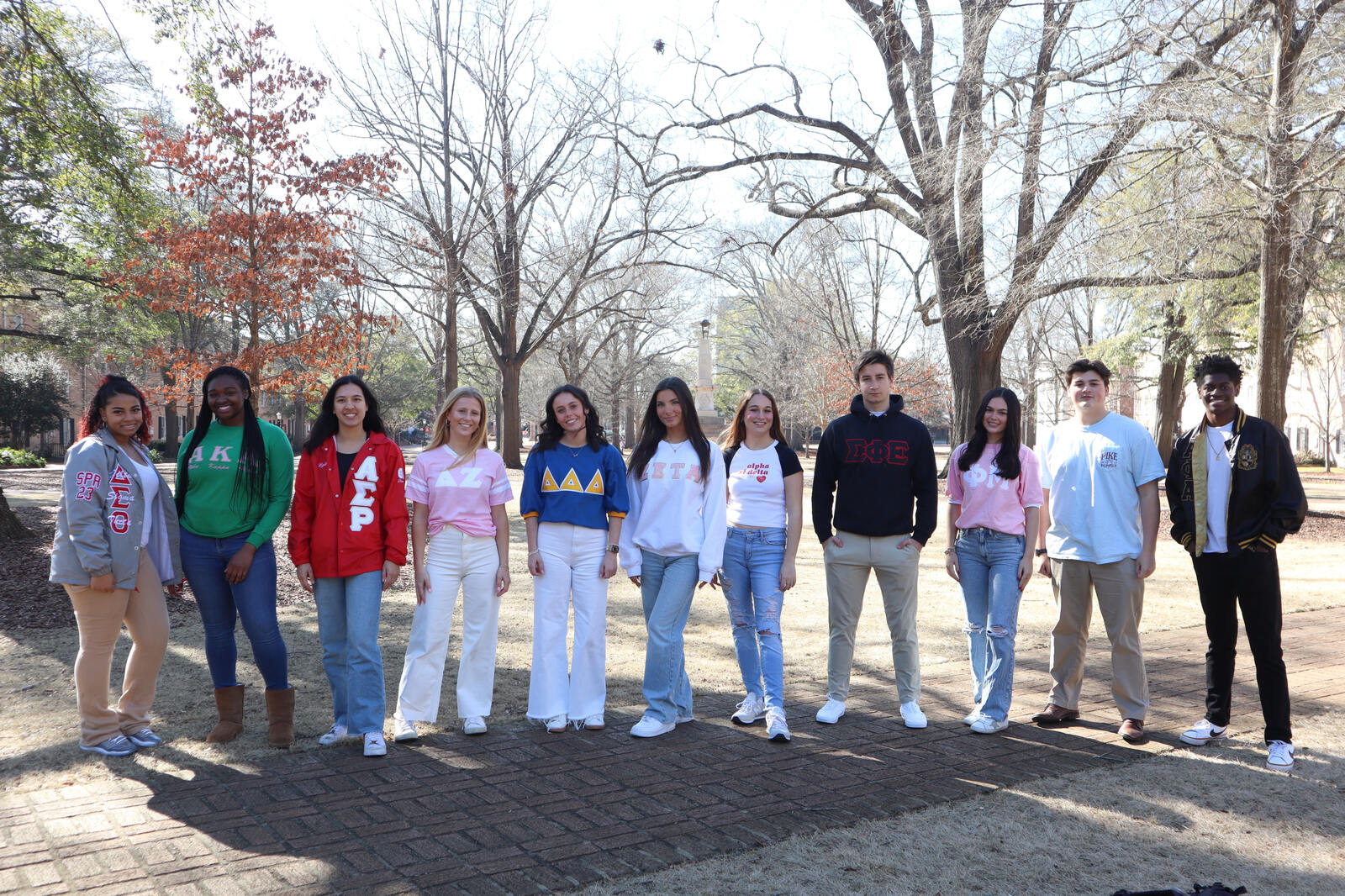 students in greek letter shirts pose in front of cocky statue