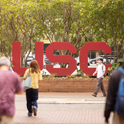 Students gather outdoors near large garnet USC letters on campus.