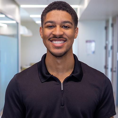 Portrait of a smiling student standing in a hallway on campus.