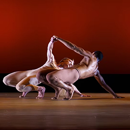 Dancers performing an expressive contemporary dance lift on stage.