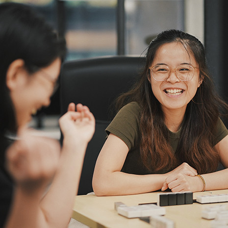Two women sit at a table, smiling and laughing