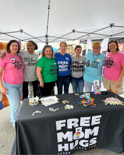 Free Mom Hugs members at a tabling event under a tent 