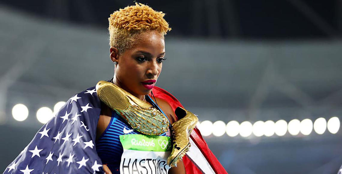 Black woman with gold track shoes and an American flag across her shoulder.