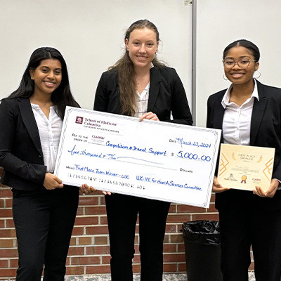 Three students holding large check and certificate