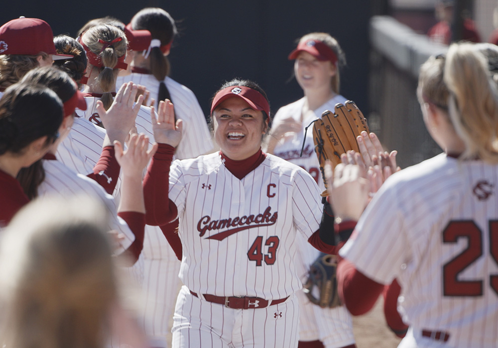 A softball player high-fives her teammates.