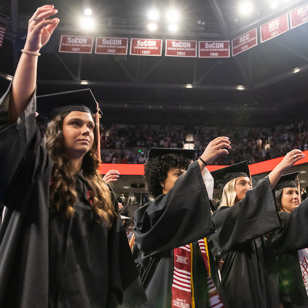 group of students holding arms up as a toast while wearing graduation robes