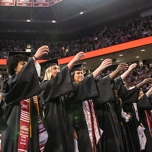group of students holding arms up as a toast while wearing graduation robes