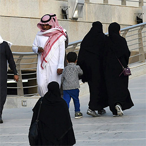 Saudi citizens wearing traditional loose robing in black and red stroll an elevated sidewalk