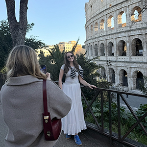 A person takes someone's picture in front of the Colosseum in Rome.