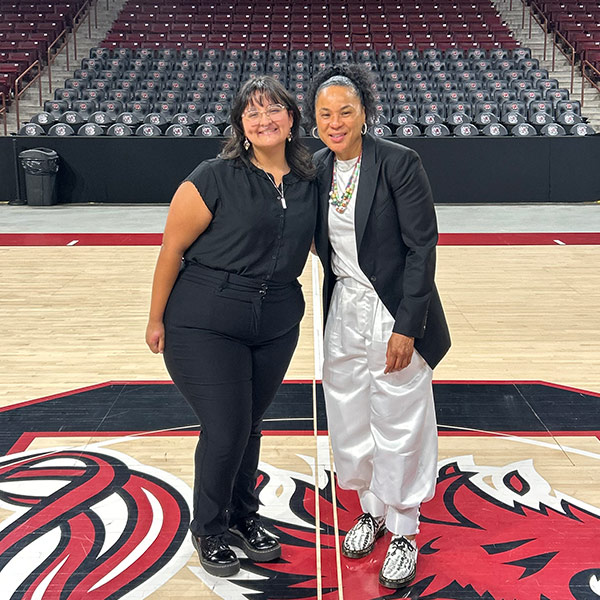 Nicole Gomez-Peele stands on the basketball court with Dawn Staley