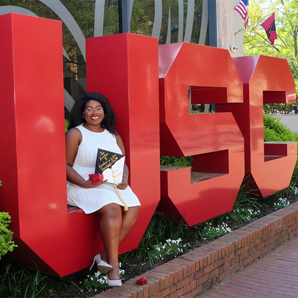 Ny'Kendria Elder sits on the garnet USC letters on campus.