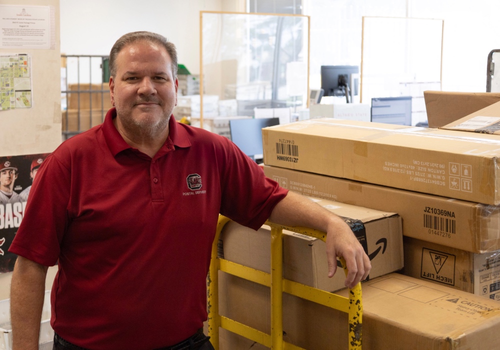 Marc Johnson poses for a portrait in front of packages at the postal services center.